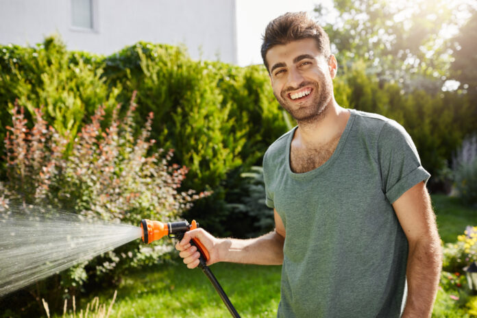 close-up-outdoors-portrait-young-good-looking-caucasian-male-gardener-smiling-watering-plants-spending-summer-countryside-house