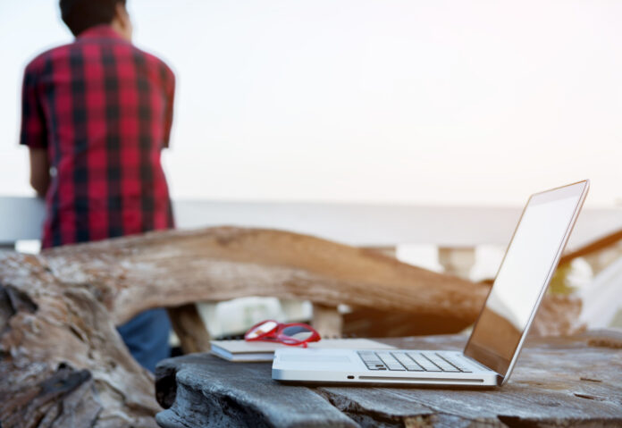 man-standing-with-laptop-glasses-wood-desk