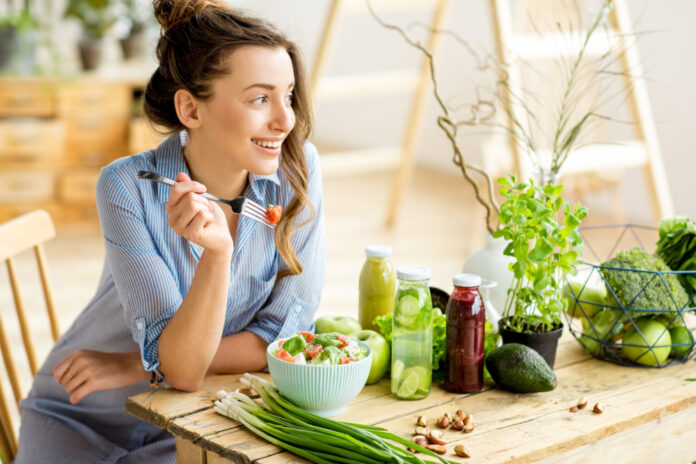young-happy-woman-eating-healthy-salad-sitting-table-with-green-fresh-ingredients-indoors
